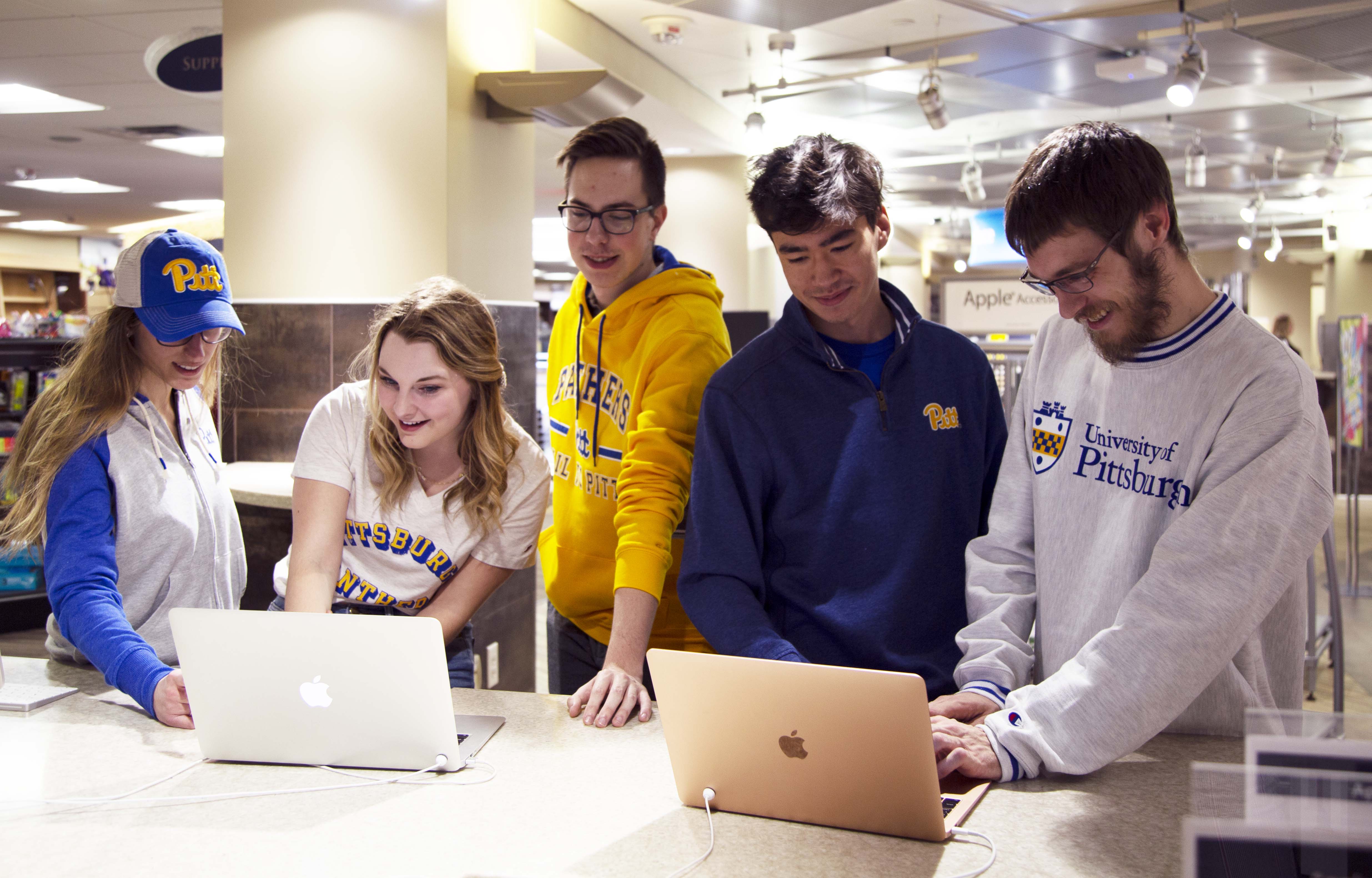 group of students leaning over Mac laptops